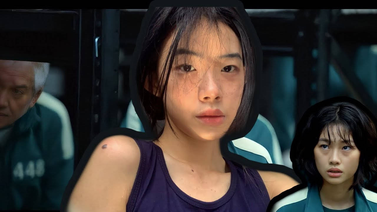 韓國士兵三別克下士 壁紙 — 一位身穿紫色背心的年輕女性，戴著黑色連帽，表情嚴肅地直視前方，在昏暗的工業環境中被另外兩個人夾在中間。