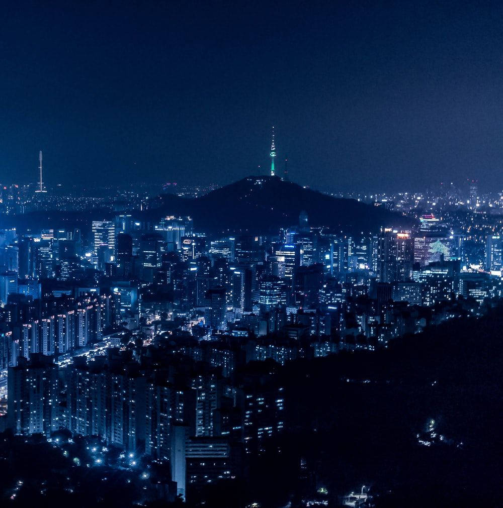 城市夜景，有發光的建築物和一座帶有發光塔樓的山。
