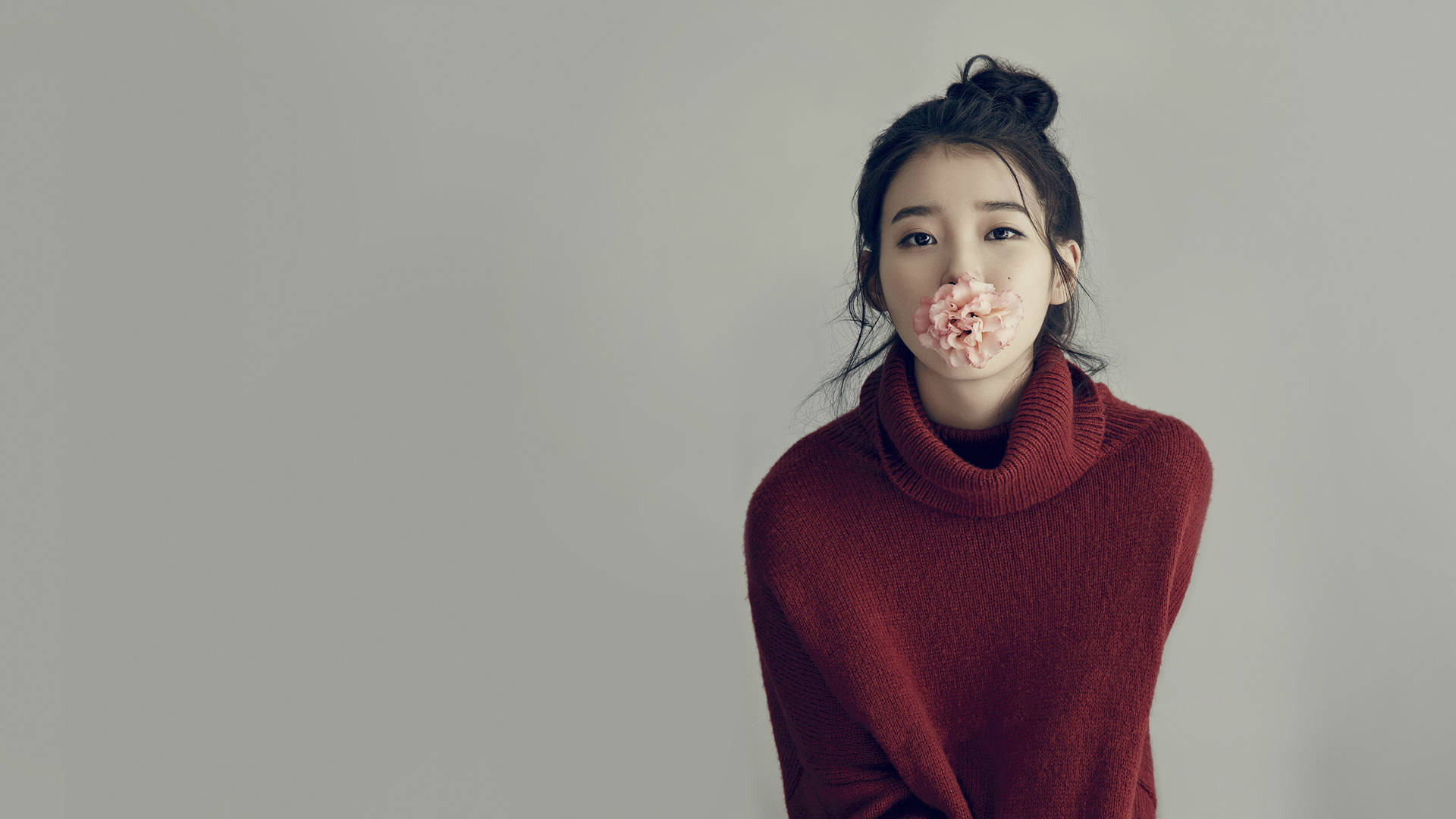 穿紅色毛衣的女性在攝影棚內將粉紅花放在嘴上