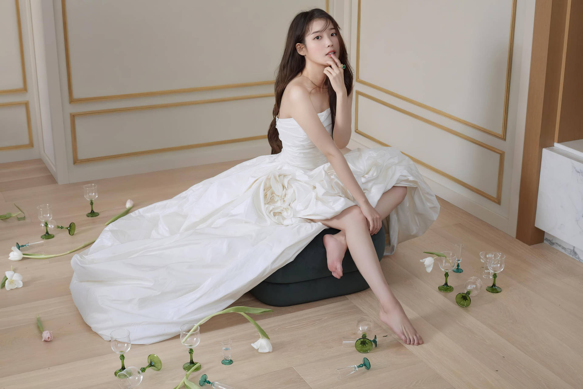 身穿白色長裙的女性赤腳坐在破碎酒杯和鬱金香之間的室內場景。