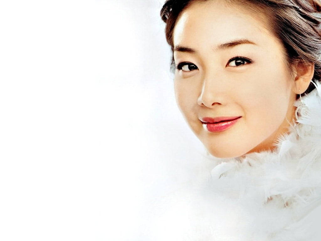 韓國女星秋瓷炫散發優雅氣質 壁紙 — 一個微笑的女人特寫肖像，她有深色眼睛和紅唇，穿著白色羽毛領，背景是明亮的白色。