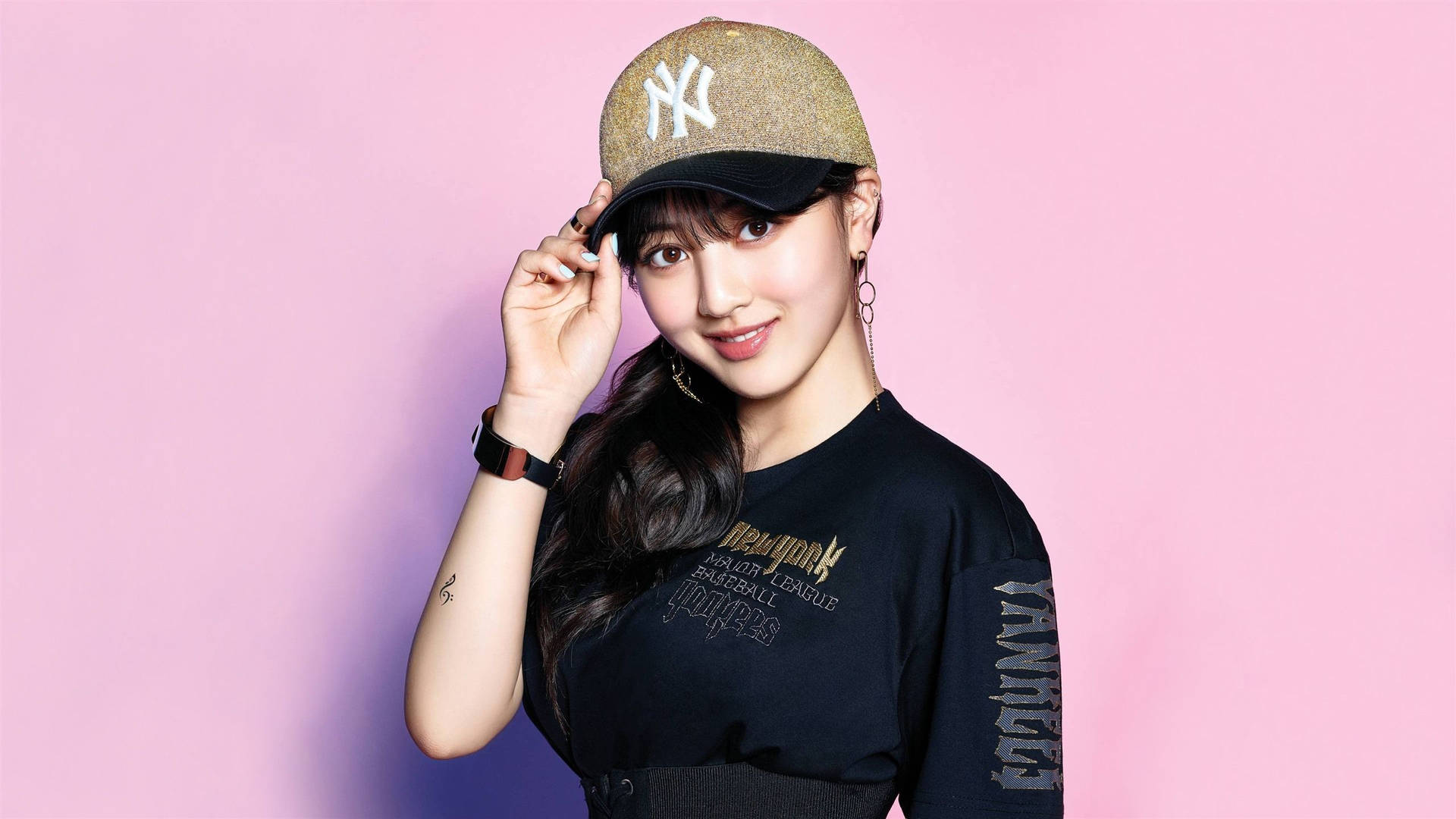 韓國女歌手Jihyo 壁紙 — 一位長黑髮的年輕女性在柔和的粉紅色背景前微笑，同時調整閃亮的洋基隊帽子。
