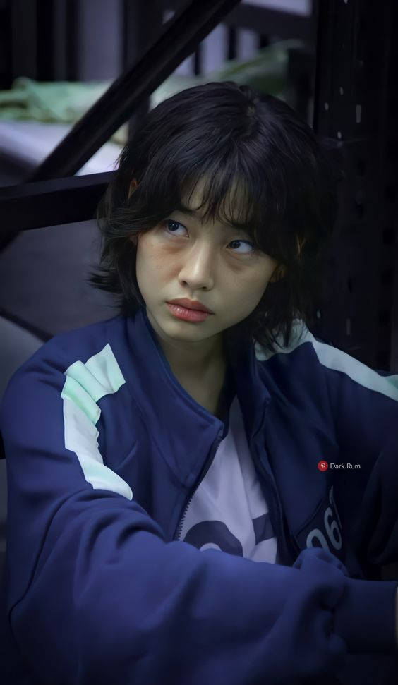 韓國女演員賽碧克身穿華麗禮服拍照 壁紙 — 一位黑髮年輕女子身穿海軍藍外套，在燈光昏暗的工業風空間中若有所思地向上凝視。
