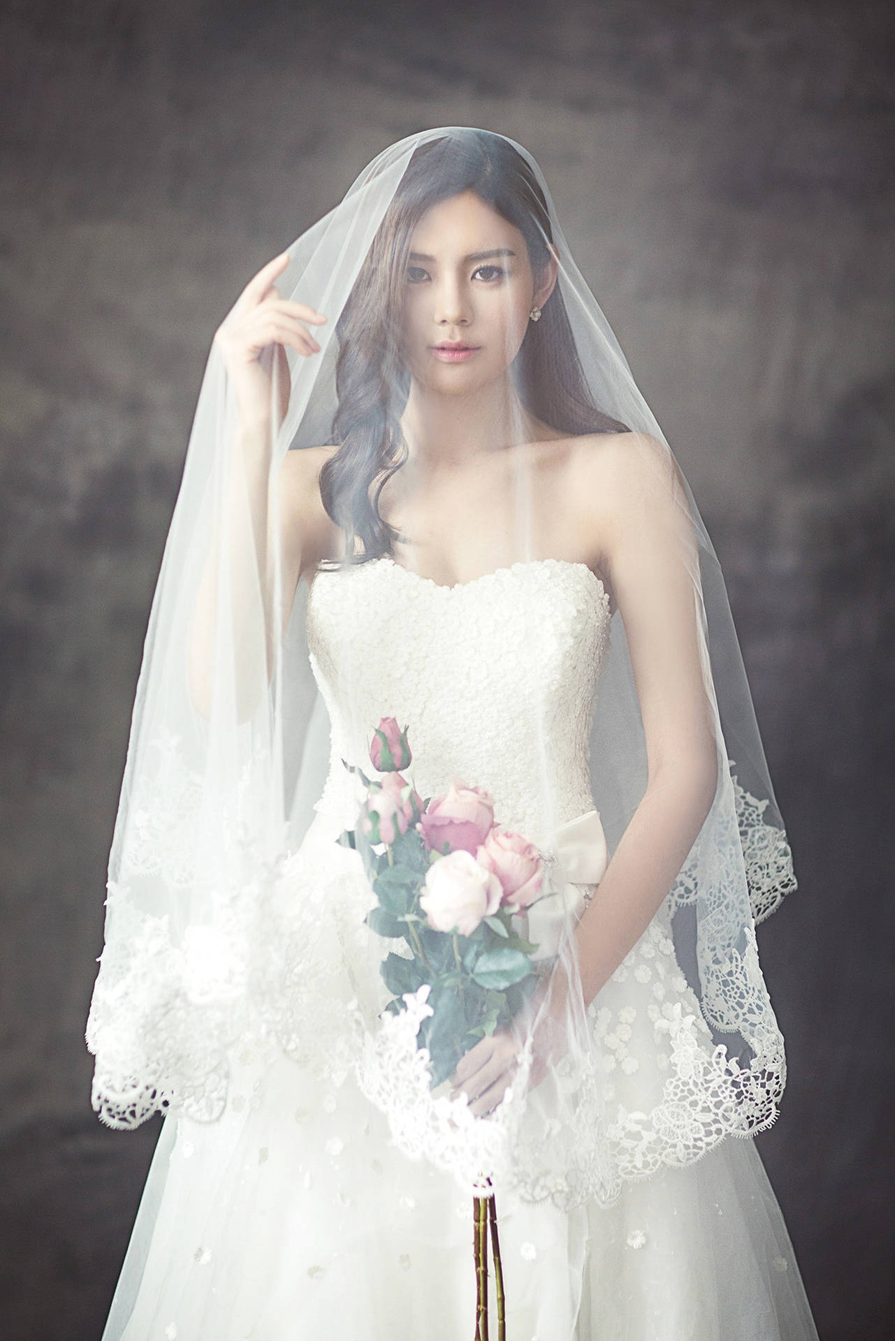 一位身穿白色蕾絲婚紗的新娘手持粉紅玫瑰。