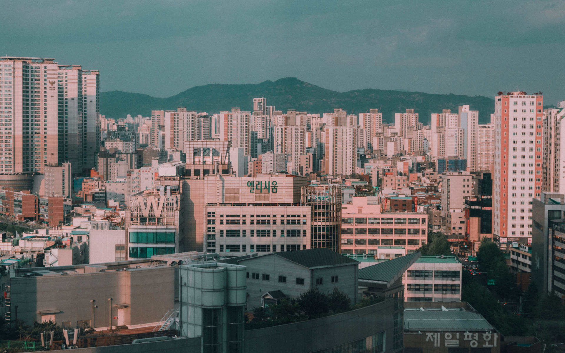 密集的城市景觀，高層建築和遠山，在藍綠色天空下。