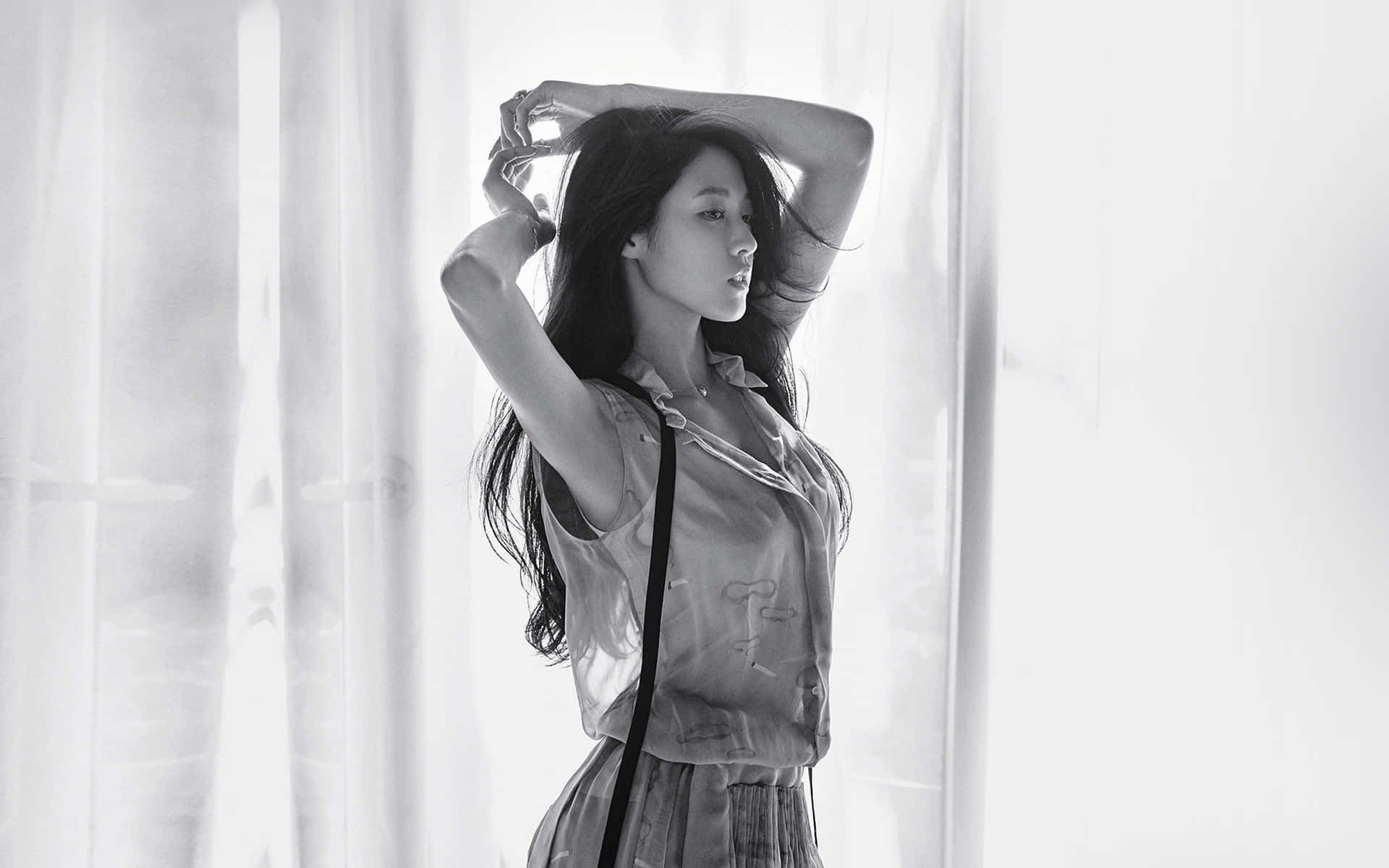 單色女性站在薄紗窗簾旁，雙臂舉起，陽光在她身後。