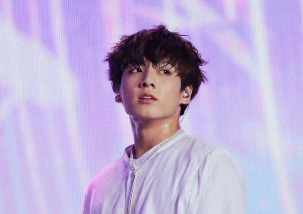 韓國歌手Jungkook目光堅定望向前方 壁紙 — 一位年輕男子，一頭凌亂的黑髮，在充滿活力的紫色和藍色舞台燈光下表演。