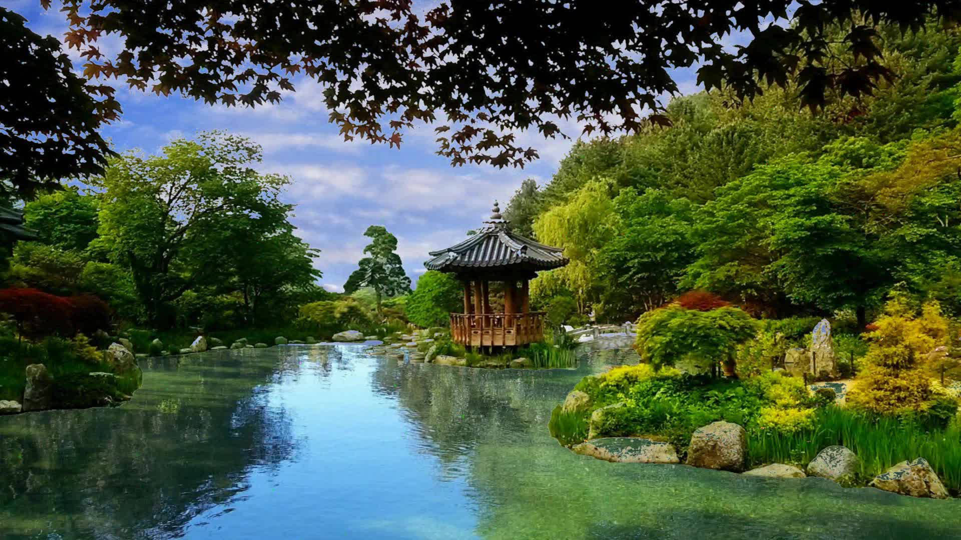 韓國湖畔花園 壁紙 — 一個寧靜的日本花園池塘倒映著傳統的木造亭子，周圍環繞著茂密的綠植和秋日樹木，上方是明亮的藍天。