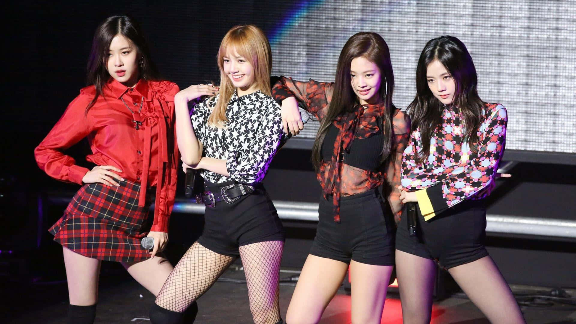韓國熱門女子團體 BLACKPINK 奪取舞台 壁紙 — 四位女K-pop偶像在燈光明亮的舞台上自信擺姿勢，穿著大膽圖案服裝和魚網絲襪。