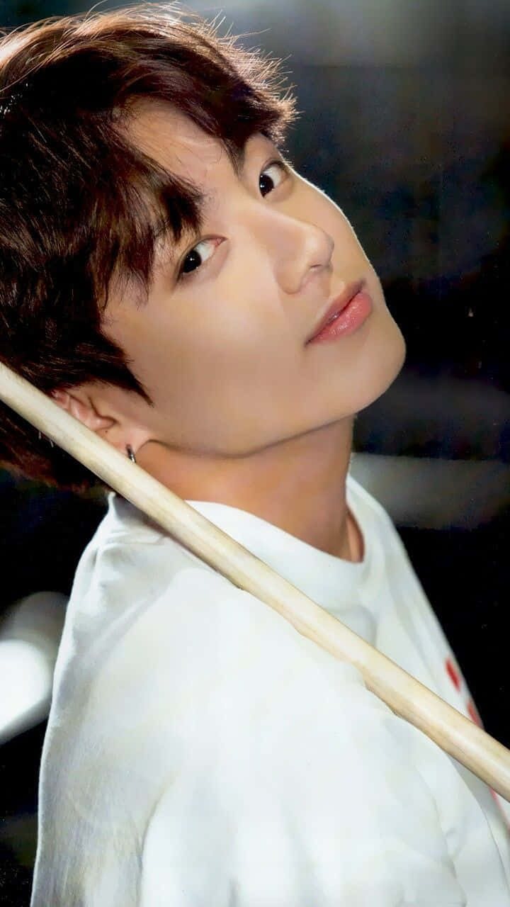 韓國男子團體BTS成員正規 壁紙 — 一位棕色頭髮、身穿白恤衫的年輕男子，肩上扛著一根木棍，向上凝視。