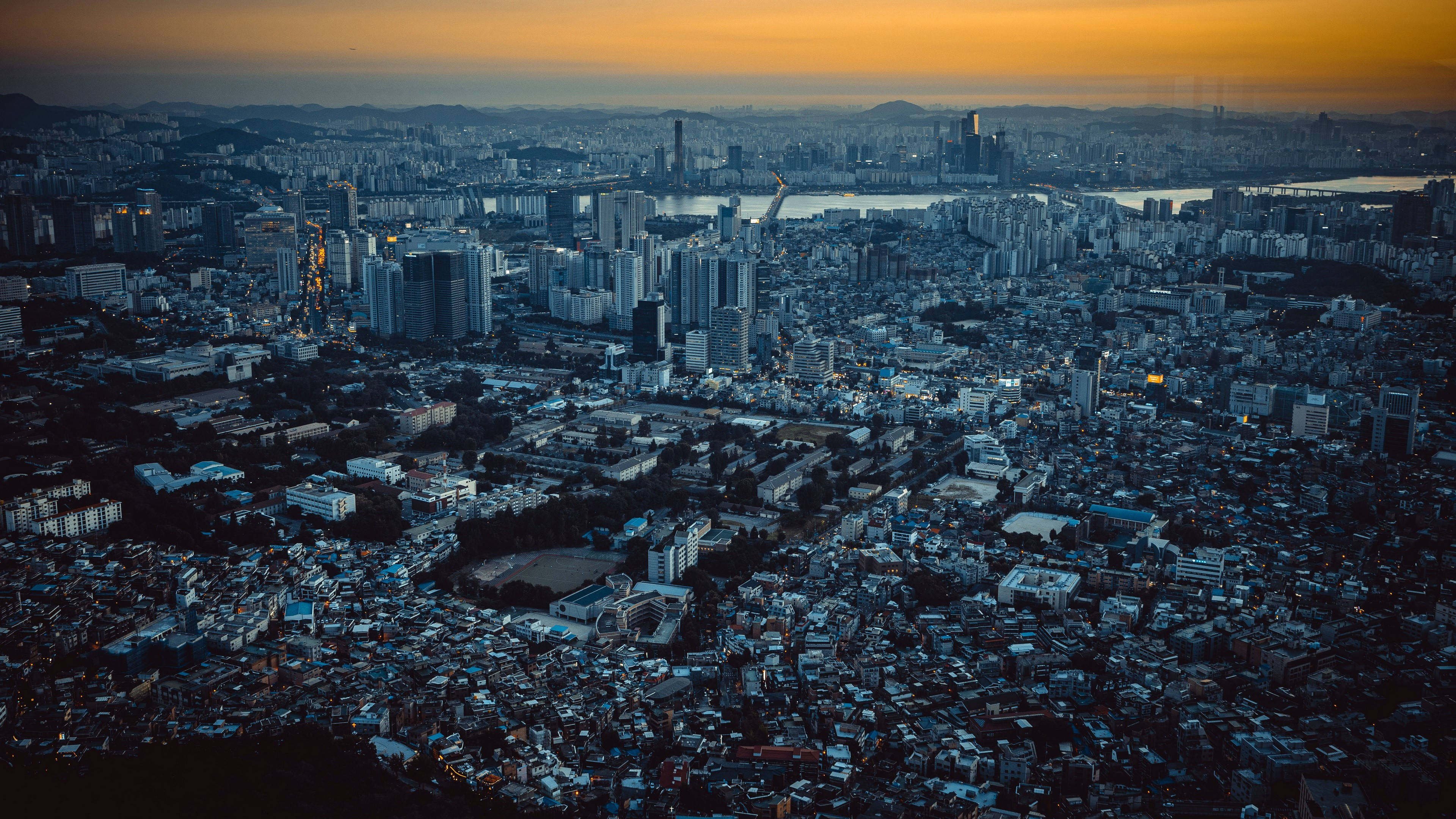 韓國首爾亞洲都市鳥瞰 壁紙 — 黃昏時分廣闊城市的鳥瞰圖，金色天空和藍色調建築。