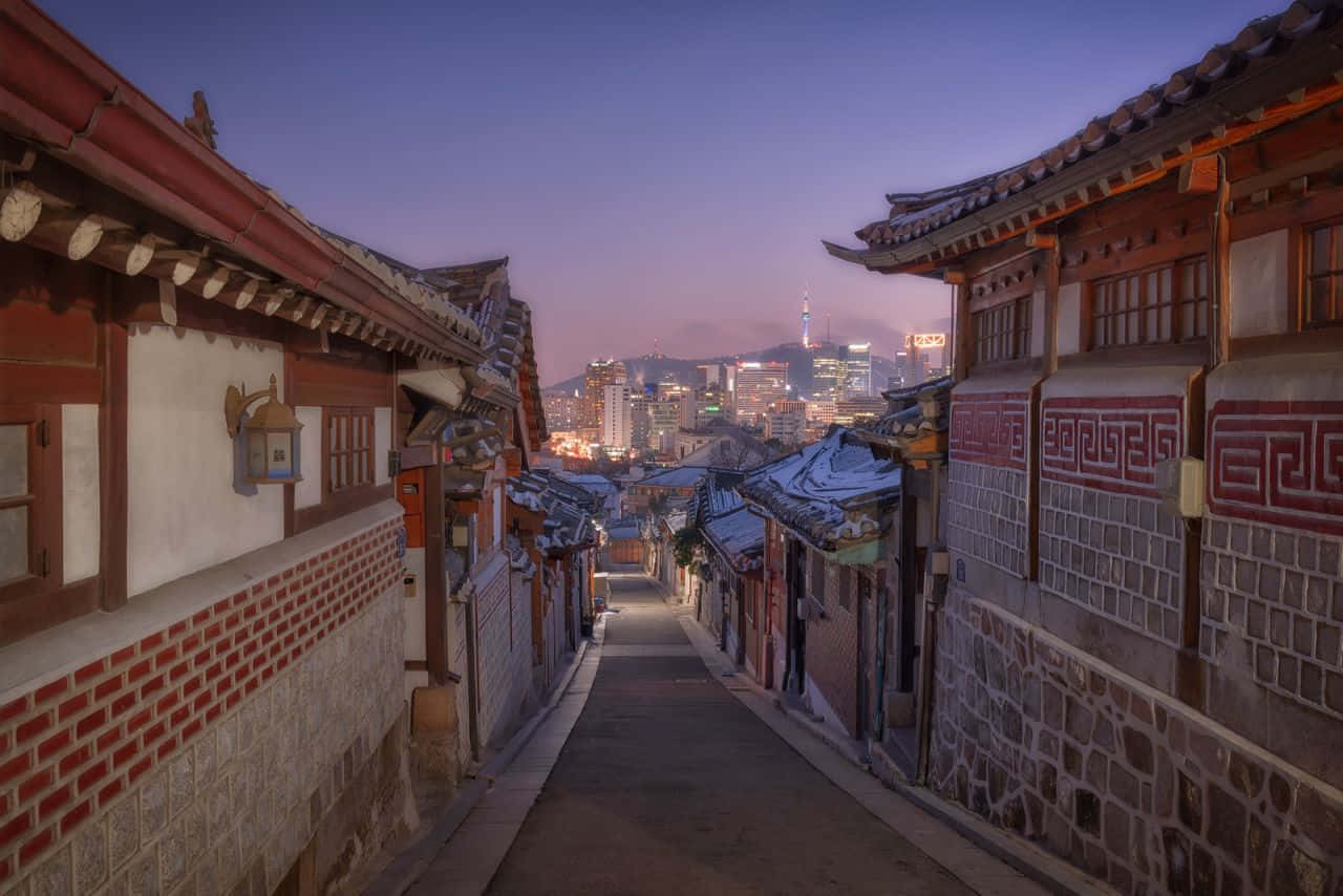 黃昏時分積雪的傳統韓國小巷，背景是現代城市燈光。