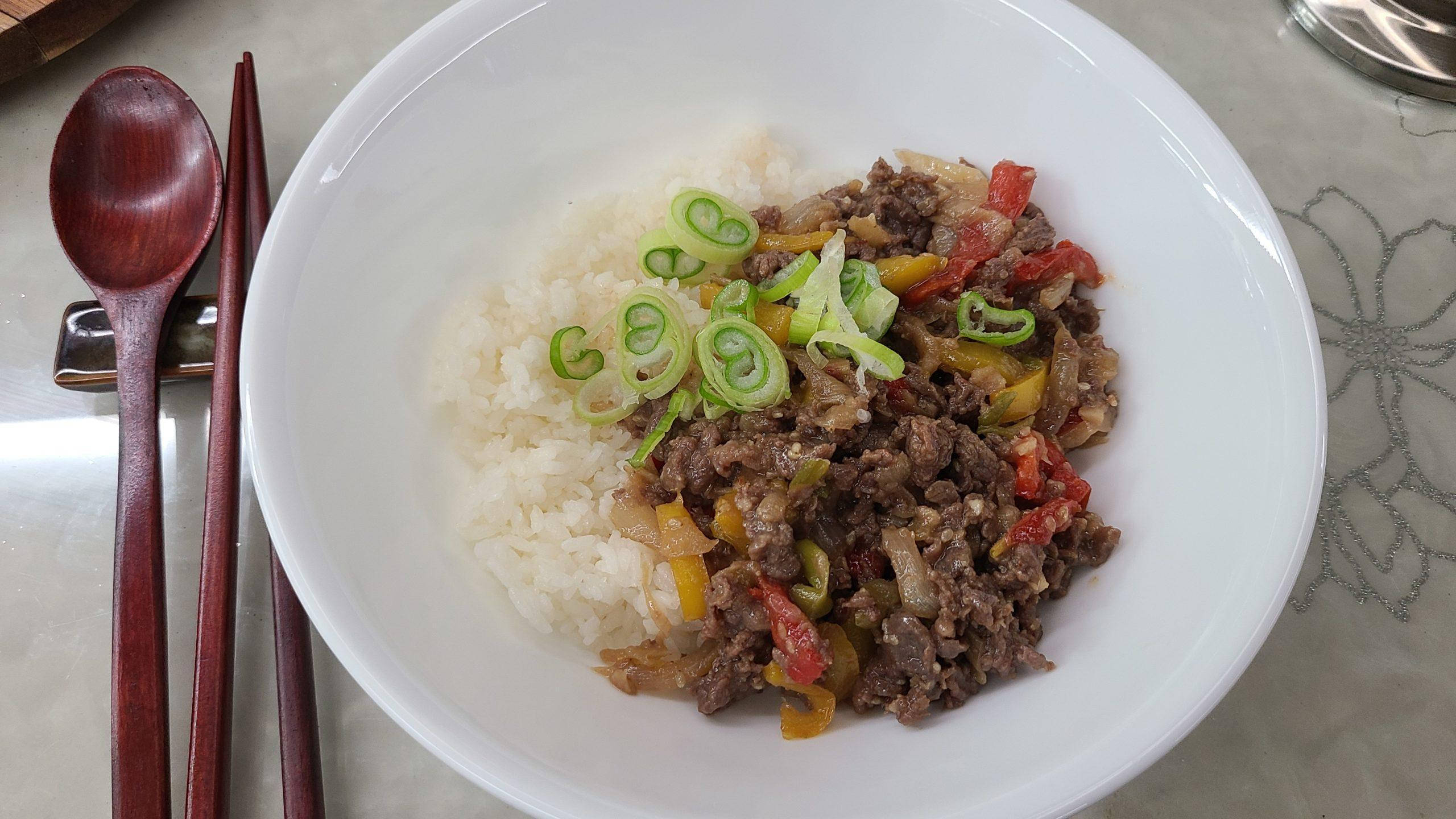 韓式醬油牛肉炒飯 壁紙 — 一個白色碗盛載蒸米飯，上面放有美味的牛肉和色彩繽紛的燈籠椒，並以切片青蔥作裝飾。