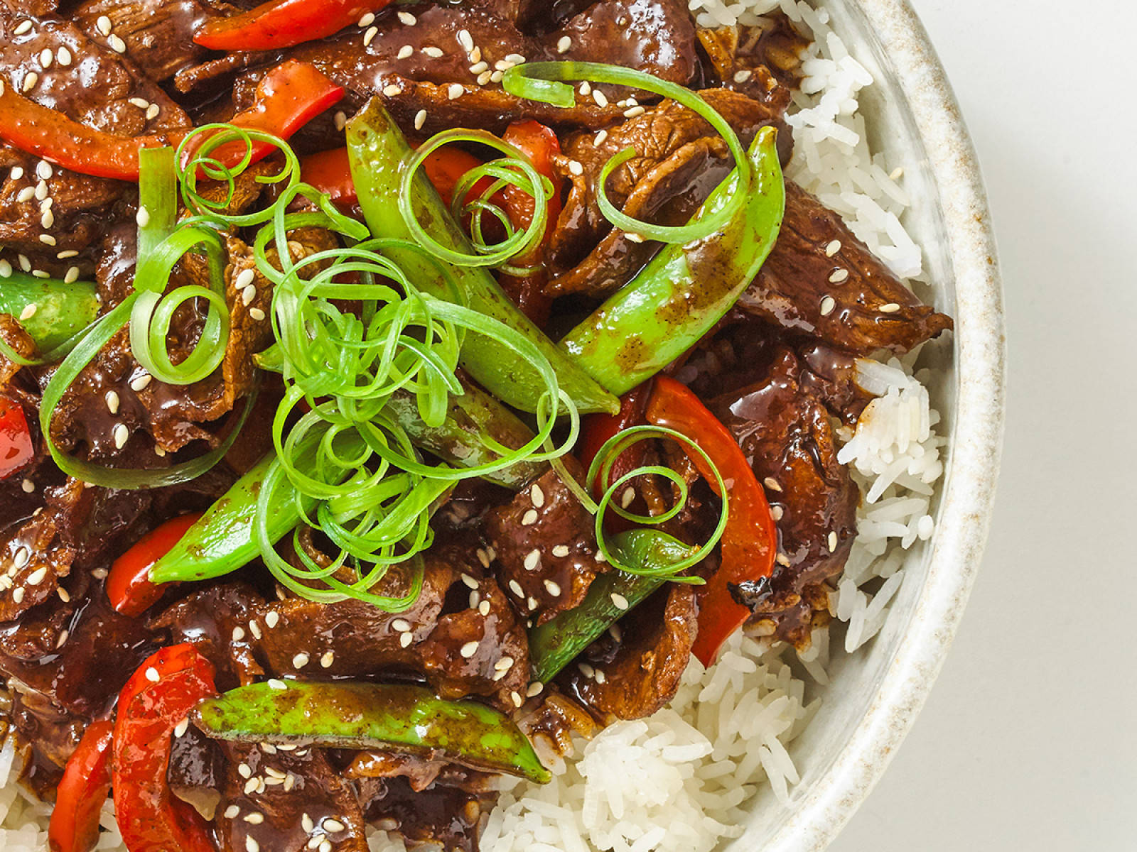 韓式醬油牛肉配白飯 壁紙 — 陶瓷碗中白飯上嘅牛肉蔬菜炒菜近鏡，有紅椒、青荷蘭豆同芝麻。