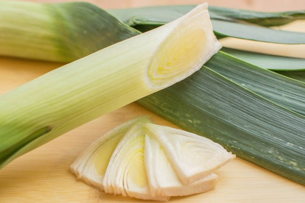 韭蔥蔬菜薄片特寫 壁紙 — 新鮮韭菜，白色根部切片，綠色葉子放在木砧板上。