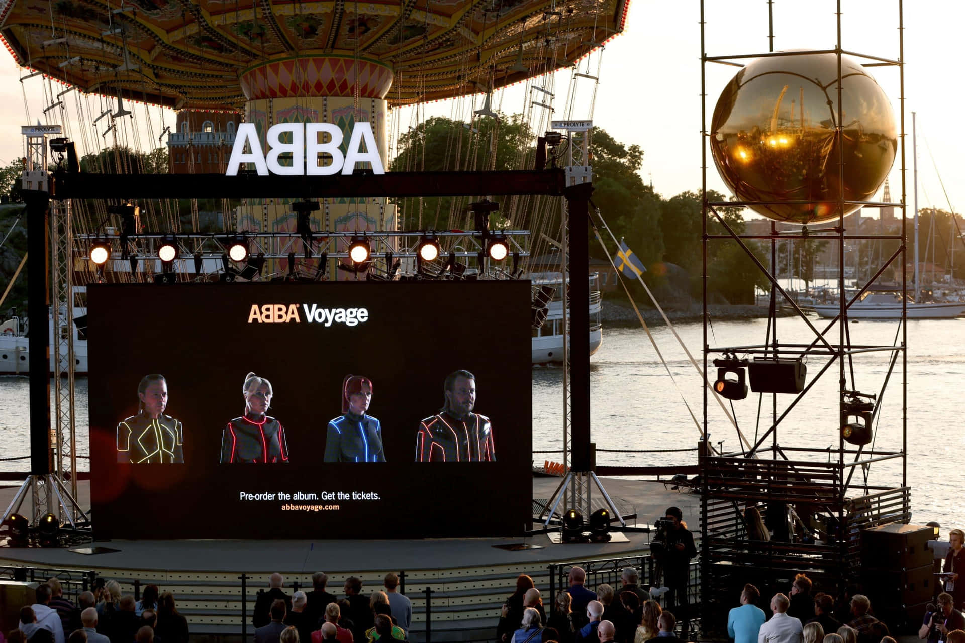 ABBA Voyage音樂會舞台，屏幕上的表演者和日落海濱的金色球體。