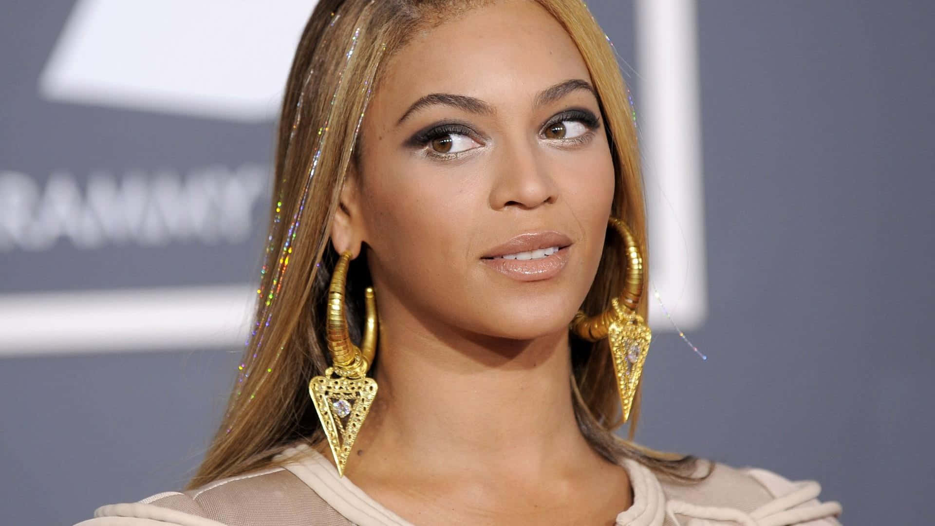 音樂女王碧昂絲 壁紙 — Beyoncé 在格林美獎上佩戴金色耳環和米色服裝，帶有閃亮的頭髮裝飾。