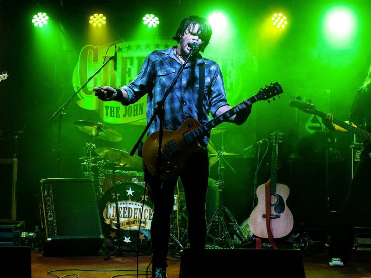 音樂家約翰·福吉提《Creedence The John Fogerty Show》演出 壁紙 — 一位音樂家在現場音樂會表演中，在充滿活力的綠色舞台燈光下熱情地彈奏結他。