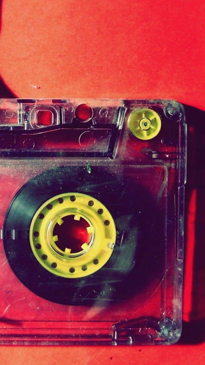 音樂響徹耳畔 壁紙 — 一盒帶有黃色捲軸的復古卡式錄音帶，在戲劇性燈光下放置於有紋理的紅色表面上。