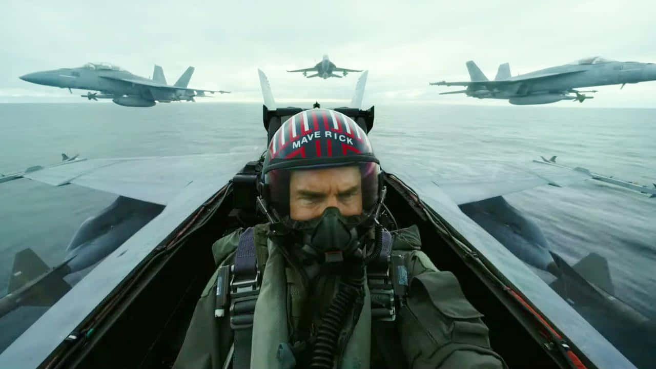 飛行員在戰鬥機駕駛艙內，三架噴射機在多雲的天空下飛越海洋。 — 頂尖飛行員： Maverick 壁紙