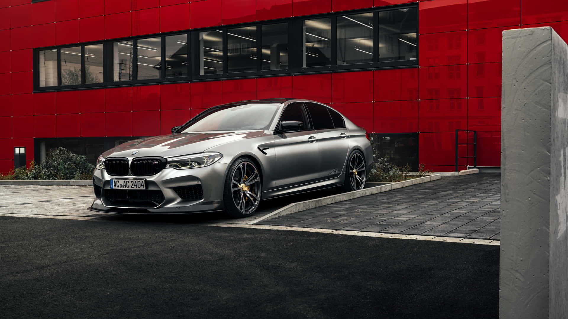 銀色BMW M5停在一棟紅色現代建築前。