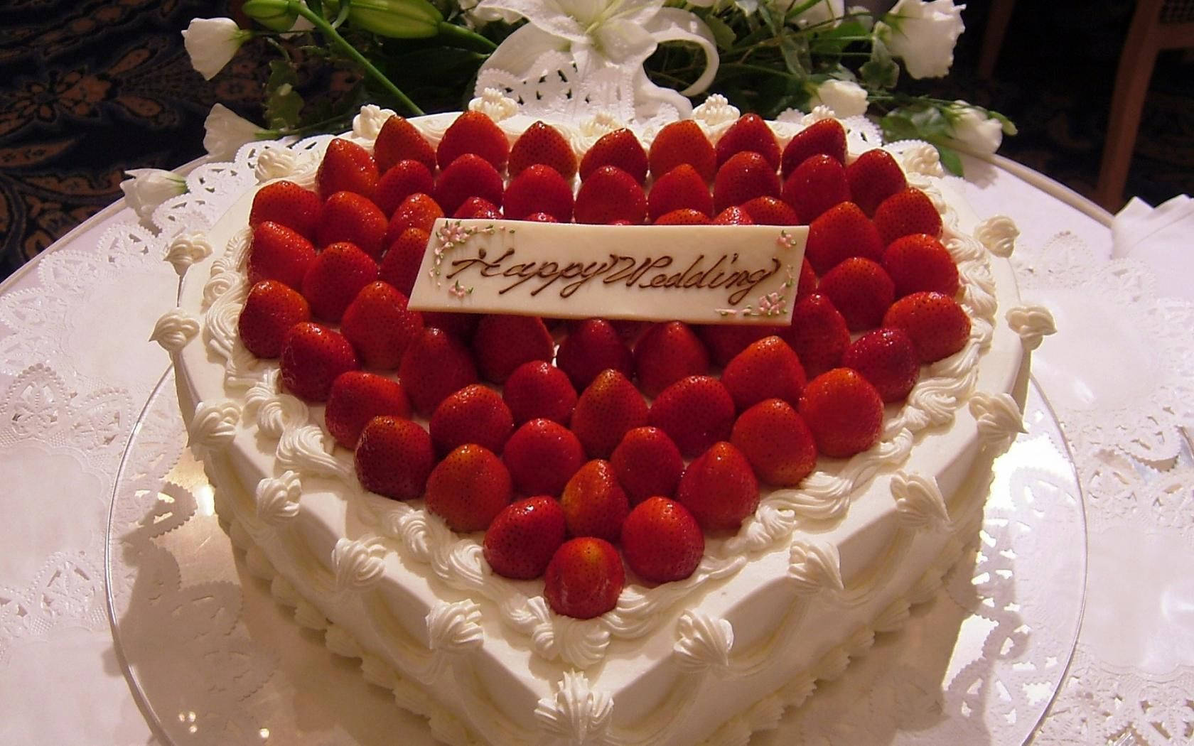 頂部裝飾草莓的生日蛋糕 壁紙 — 一個心形結婚蛋糕，飾以新鮮草莓和「Happy Wedding」牌匾，優雅地放在蕾絲桌布上。
