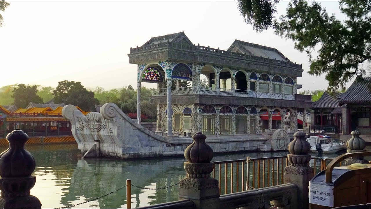 頤和園大理石船 壁紙 — 一艘宏偉華麗的石舫，雕刻精細，在平靜的水面上悠然漂浮，四周環繞著傳統中式建築和茂密的綠樹。