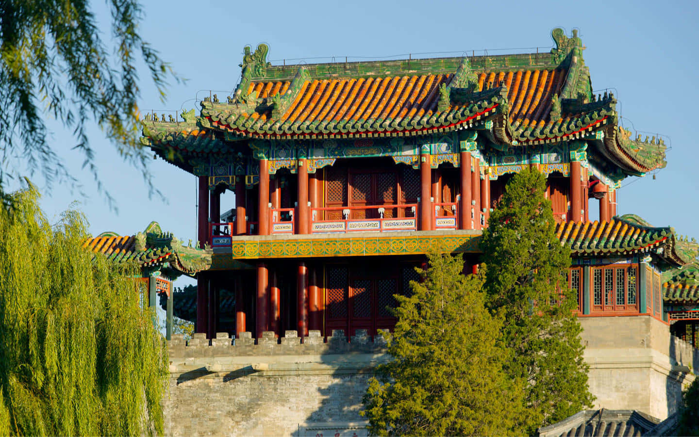 頤和園紫禁城 壁紙 — 一座傳統中國寶塔，擁有鮮豔的橙色和綠色瓦片屋頂，在晴朗的藍天下巍然聳立，四周環繞著茂密的綠樹。