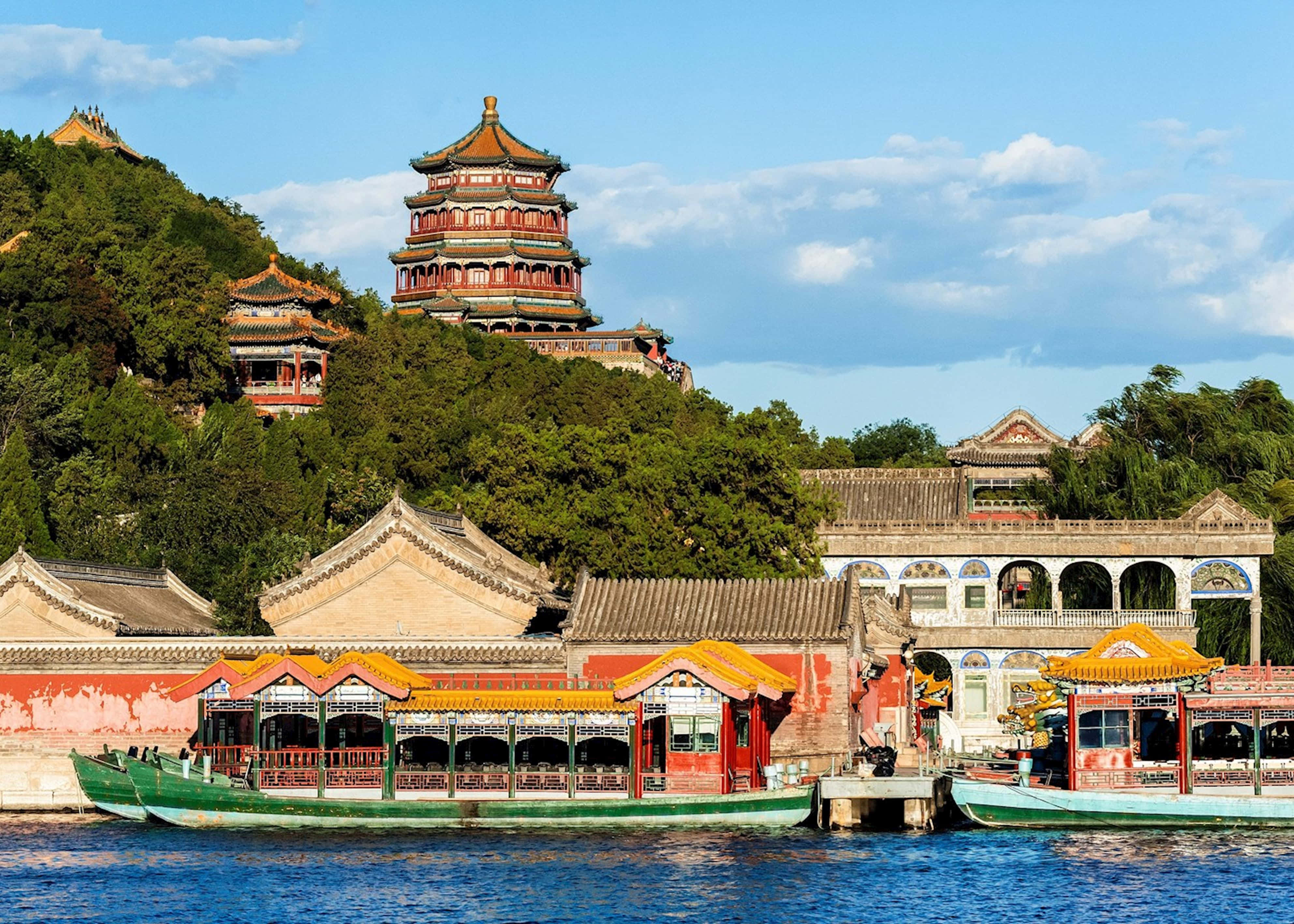 頤和園遊船 壁紙 — 傳統中國宮殿建築，紅色屋頂和綠色船隻漂浮在平靜的藍色湖面上，天空部分多雲。