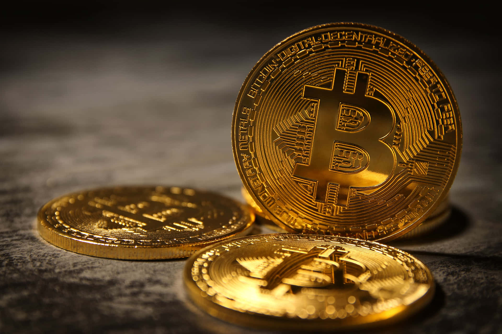 三枚金色比特幣在深色紋理表面上，聚焦燈光照射。