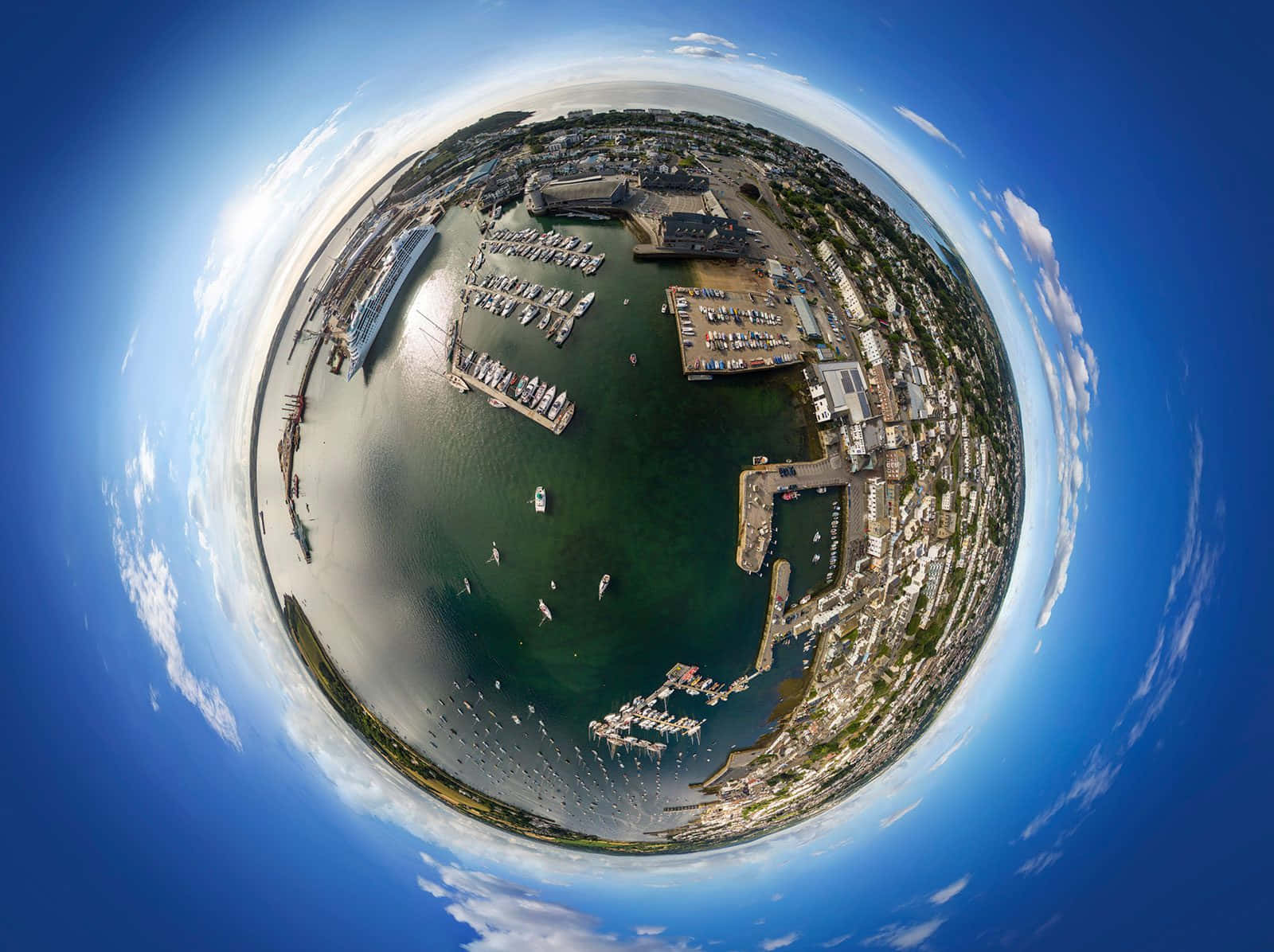 類似星球的海洋 360度全景圖 壁紙 — 一個令人驚嘆的360度魚眼視角，俯瞰海岸港口，船隻停泊，建築物環繞水面，天空湛藍明亮。