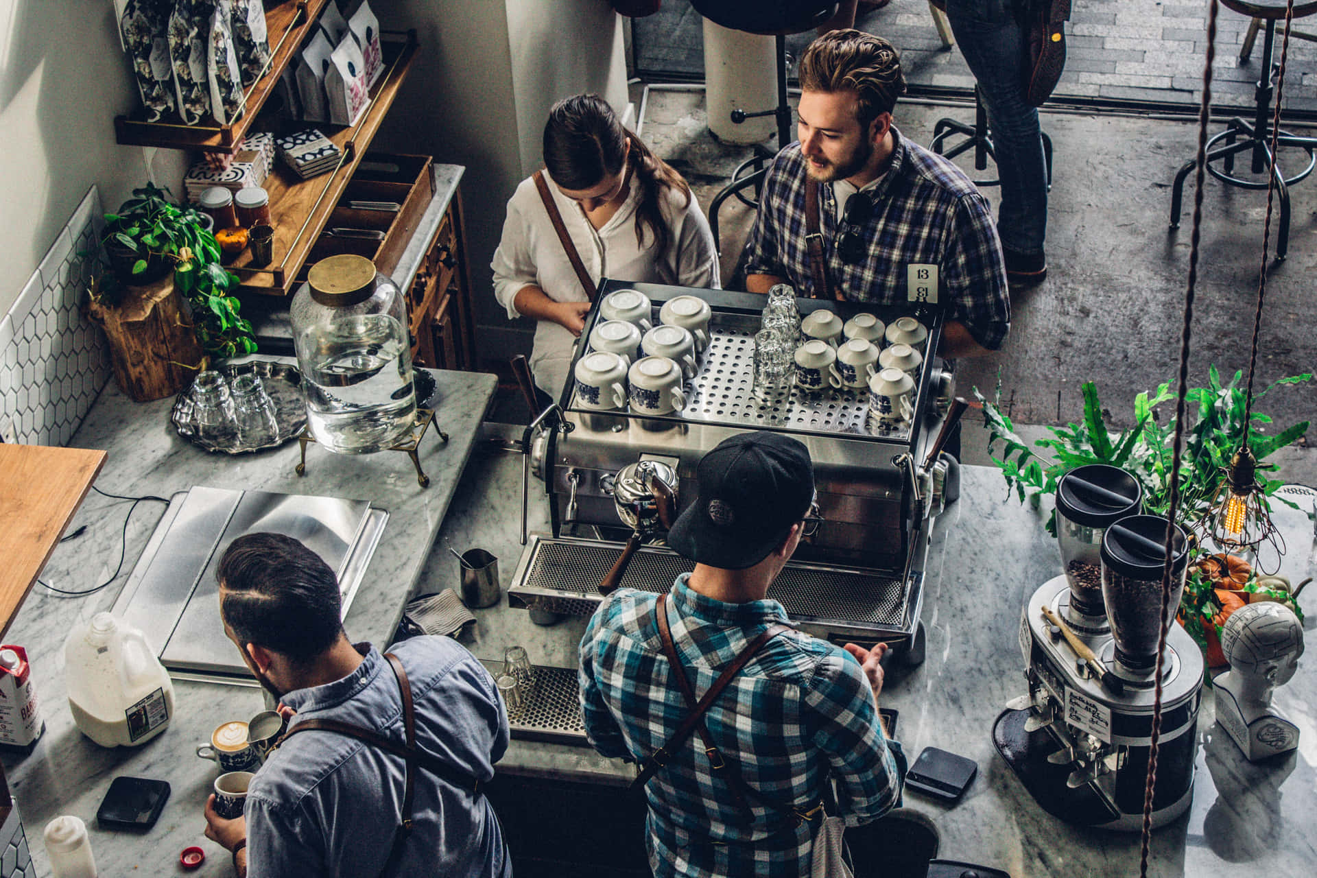 Baristas and customers at a modern coffee shop with marble counters and green plants.
