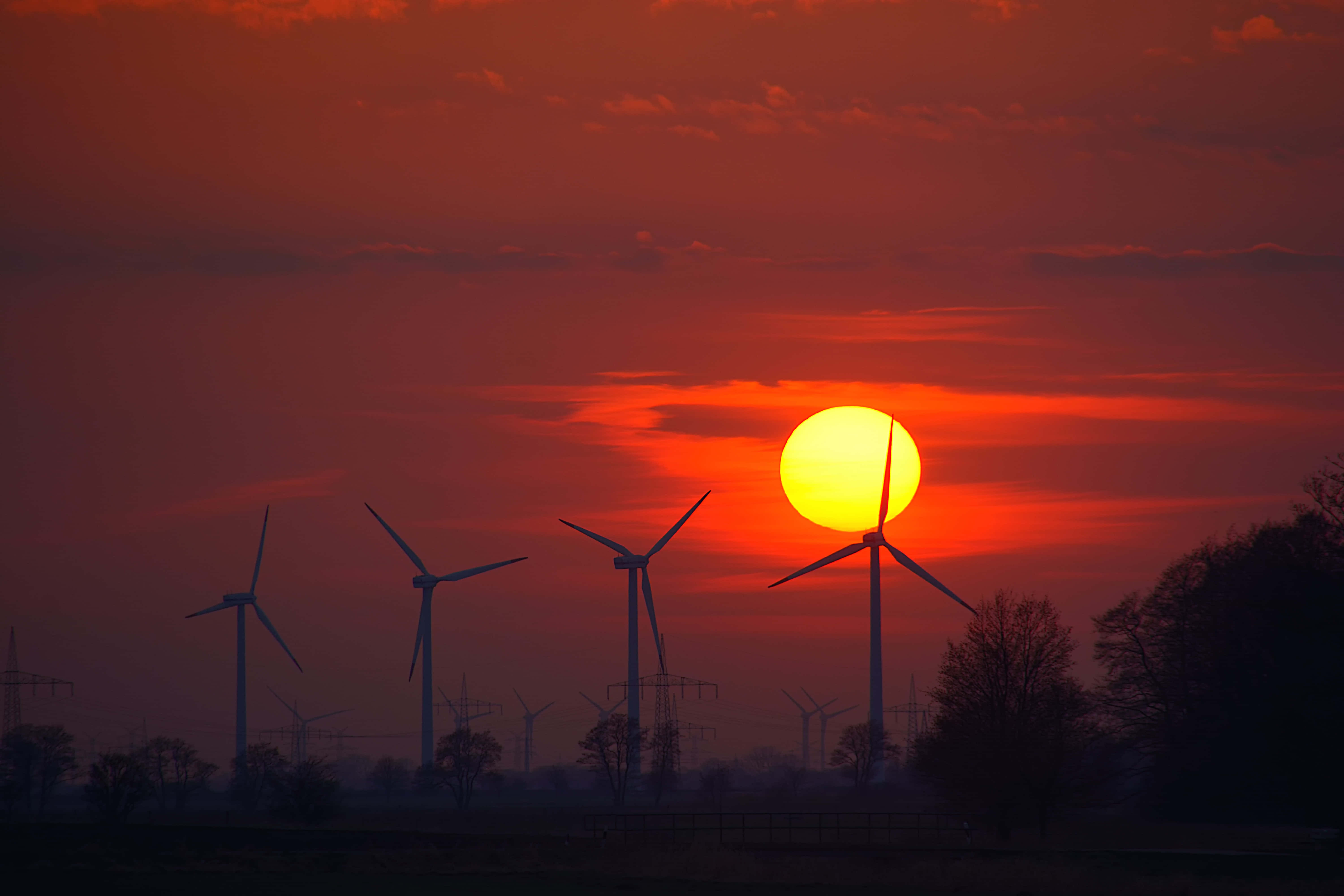 Wind 桌布 壁紙 — 風力渦輪機的剪影在火紅橙色的日落天空下聳立，伴隨著發光的太陽。