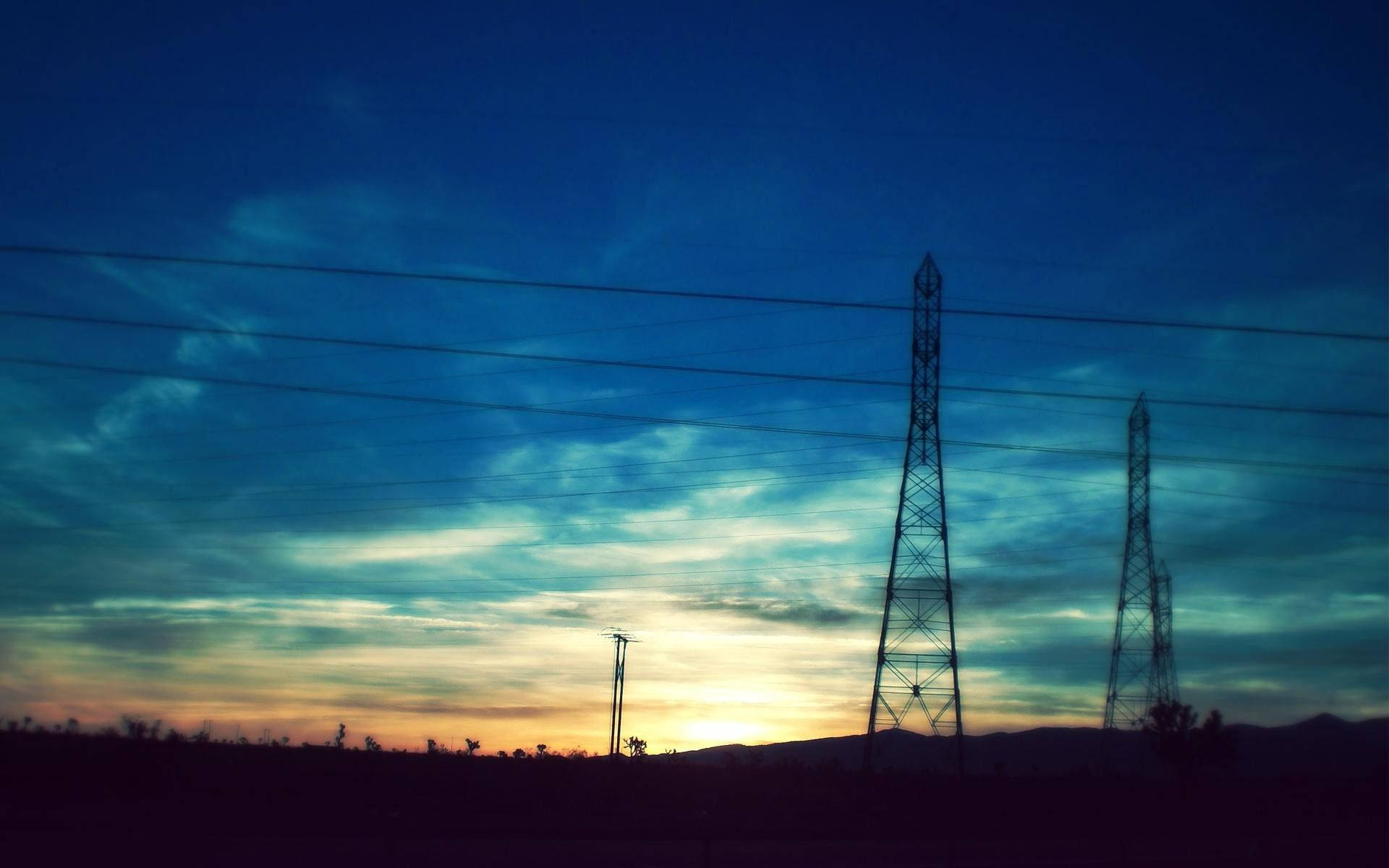風景電力塔 壁紙 — 電線塔的剪影在充滿活力的暮色天空中延伸，天空佈滿橙色和深藍色的雲彩條紋。