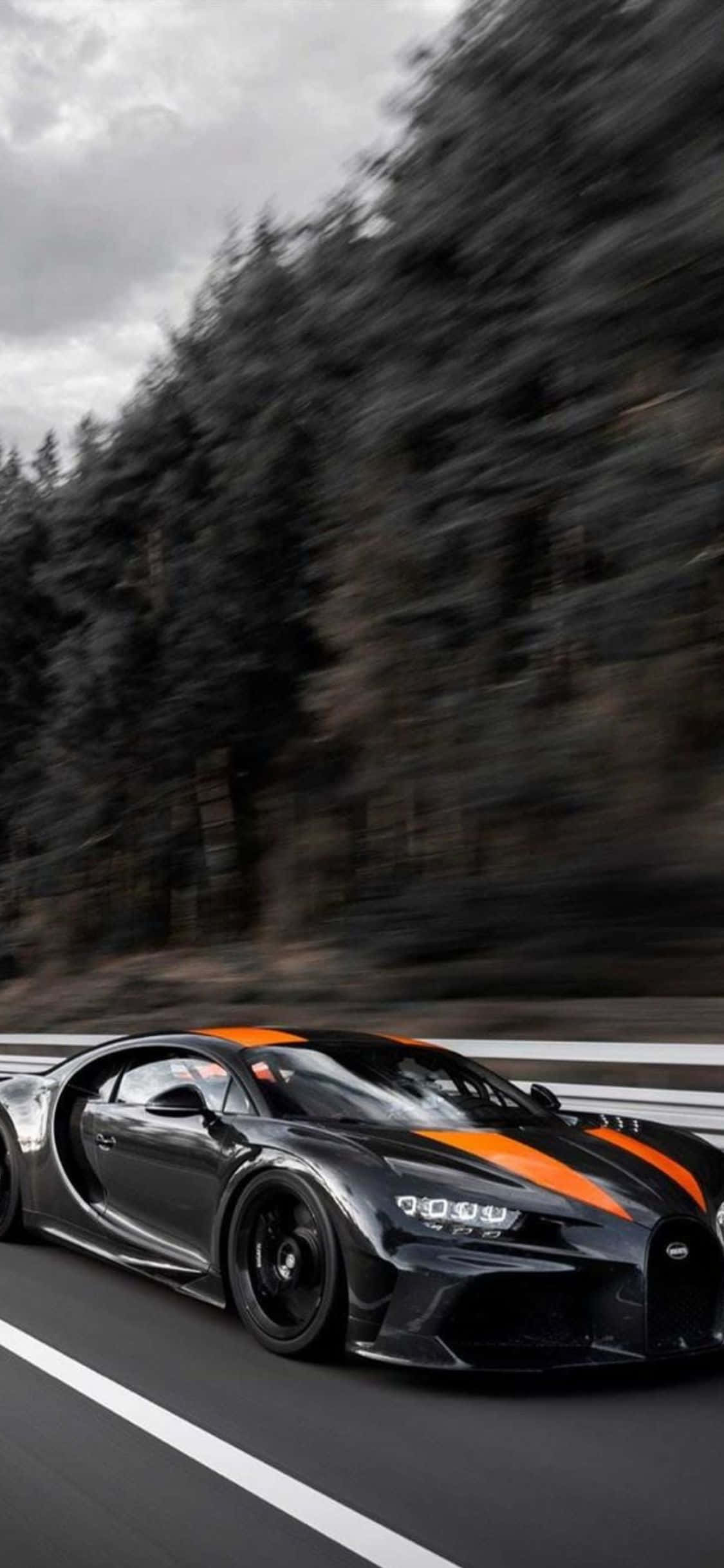風格與速度：iPhone XS與Bugatti Veyron 壁紙 — 一輛黑色 Bugatti Chiron 帶有橙色點綴，在樹林環繞的道路上行駛，帶有動態模糊效果。