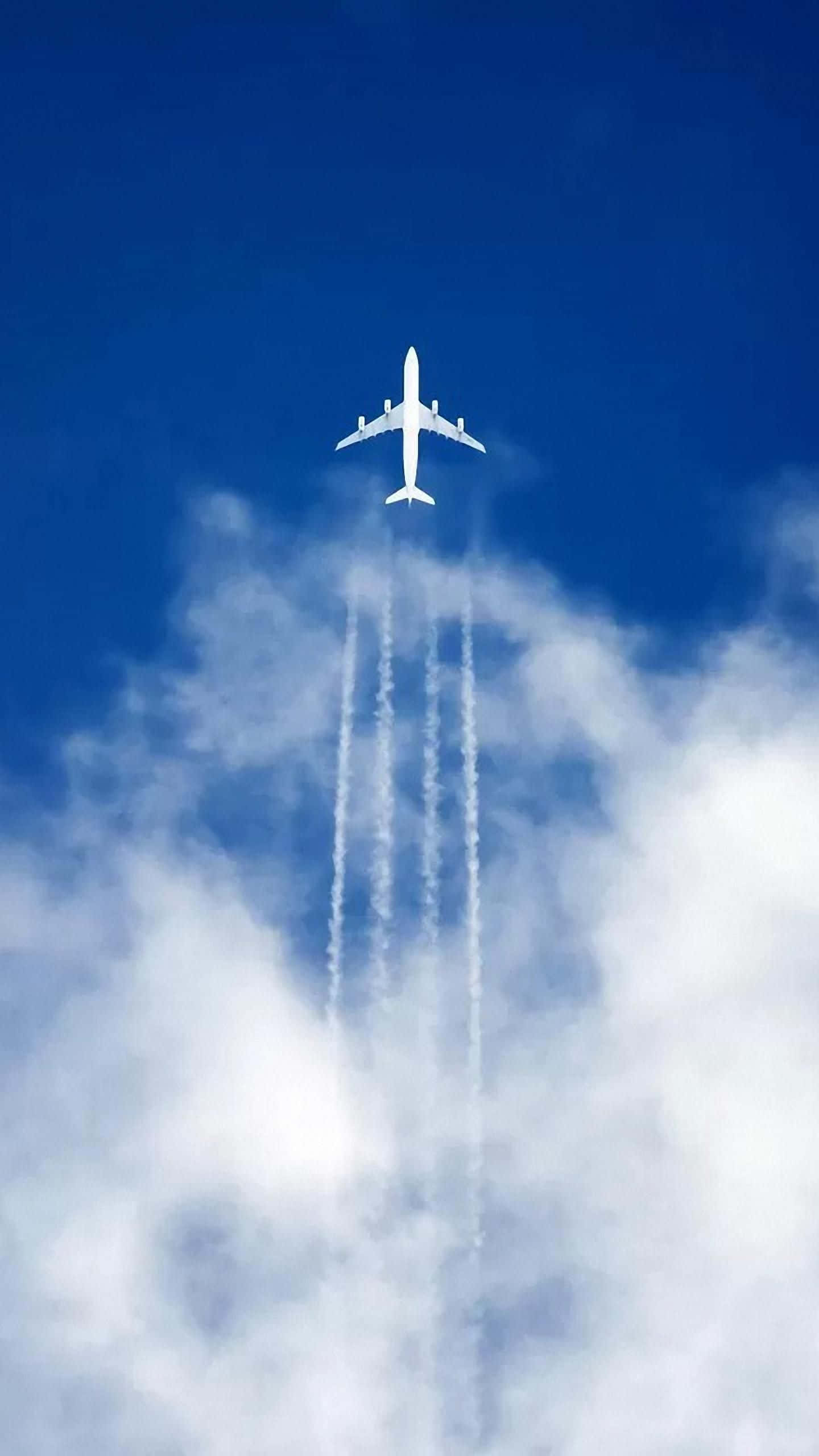 飛向天空 壁紙 — 一架白色客機在深藍色的天空中翱翔，飛過蓬鬆的白雲，留下四條明顯的凝結尾跡。