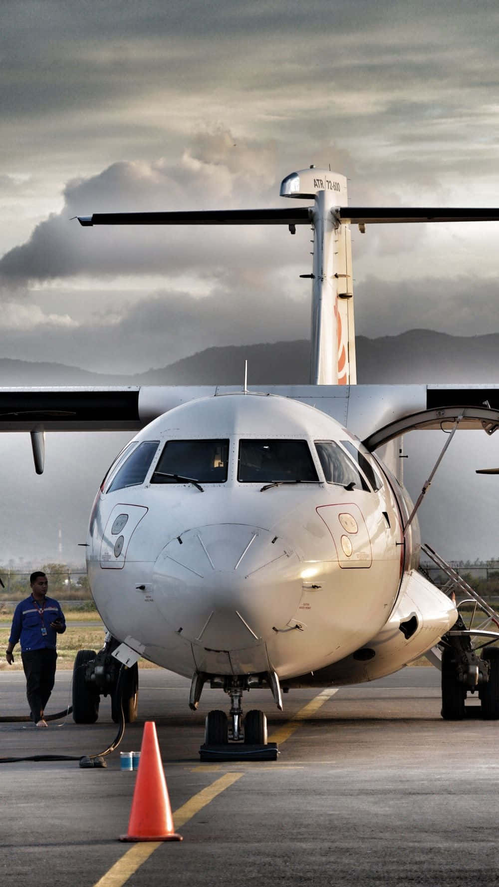 飛向天空，追逐夢想 壁紙 — 一架白色渦輪螺旋槳飛機停在停機坪上，天空多雲，背景有山脈，附近有地勤人員。