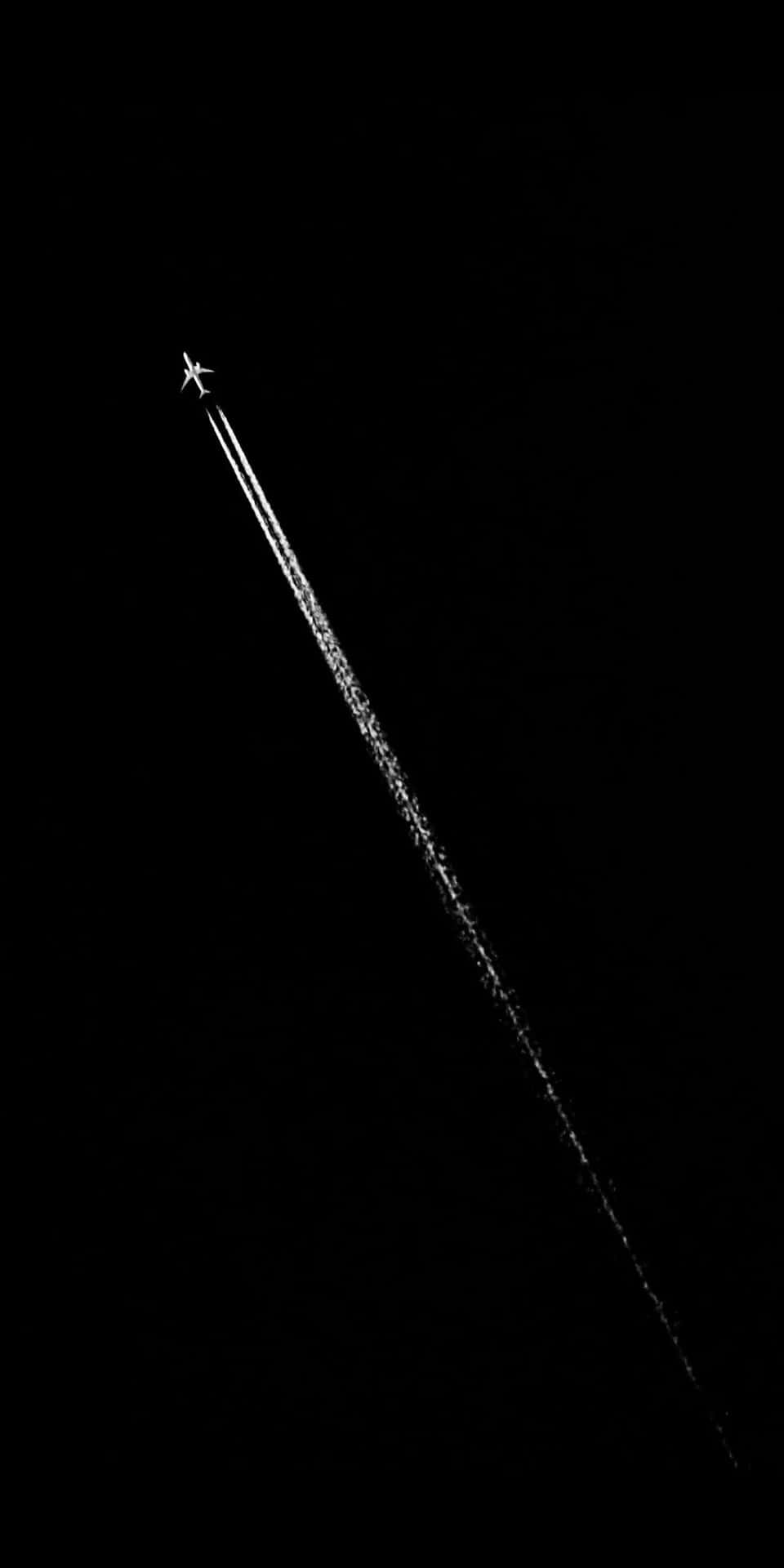 夜間飛行的飛機在黑暗的天空中留下一道長長的白色的凝結尾跡。