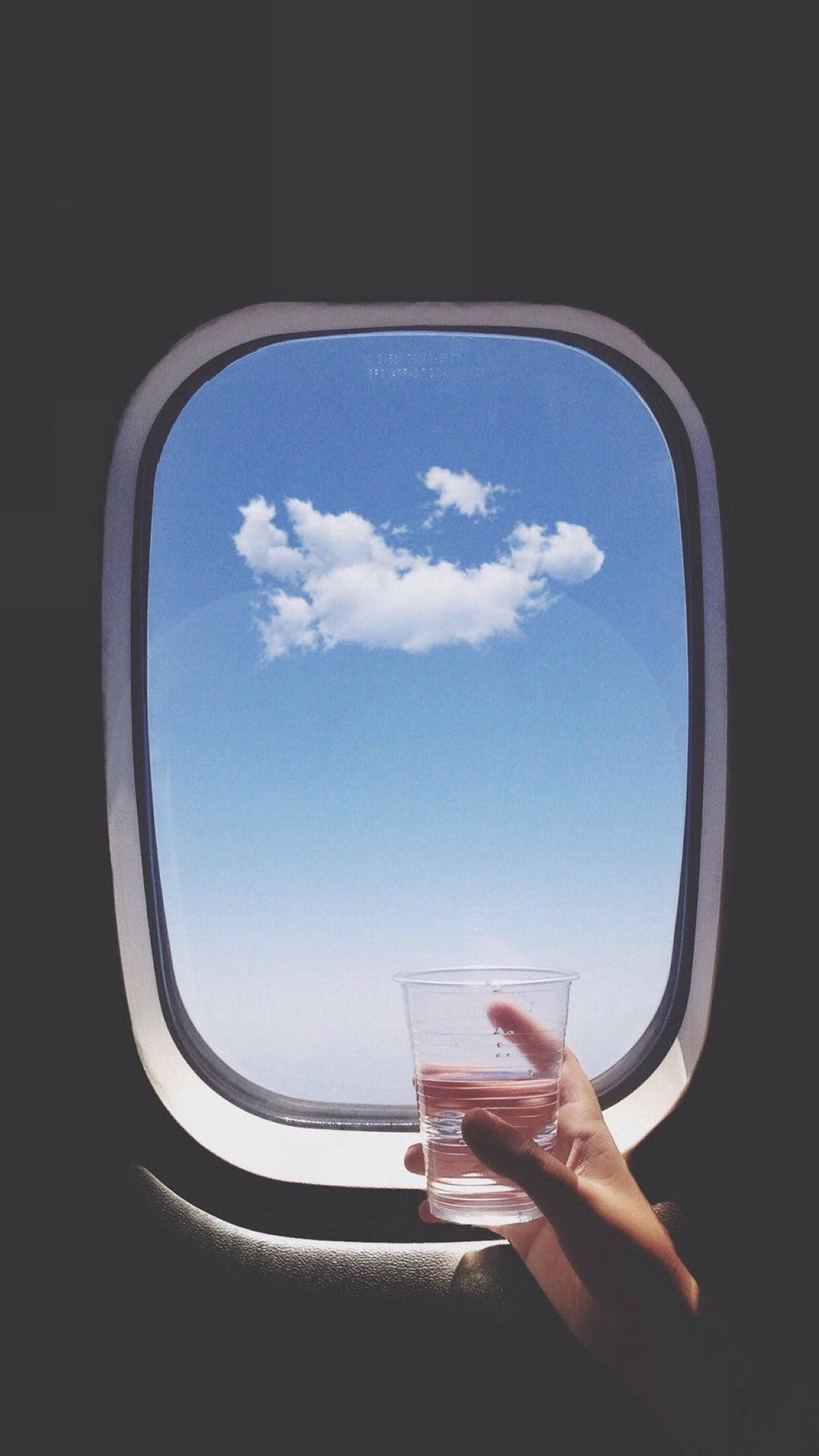 手拿水杯在飛機窗邊，看著藍天白雲