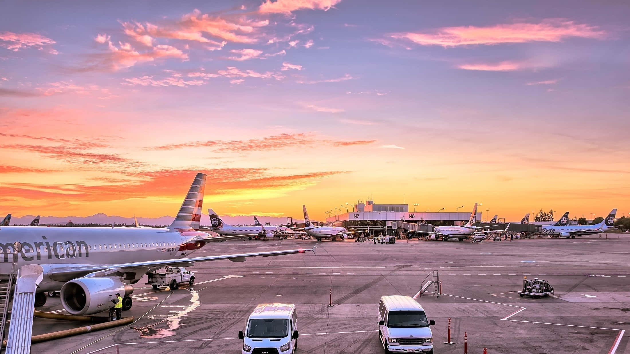 Airport 桌布 壁紙 — 飛機停泊在機場閘口，天空呈現充滿活力的日落色彩，有粉紅、橙色和紫色的雲彩。