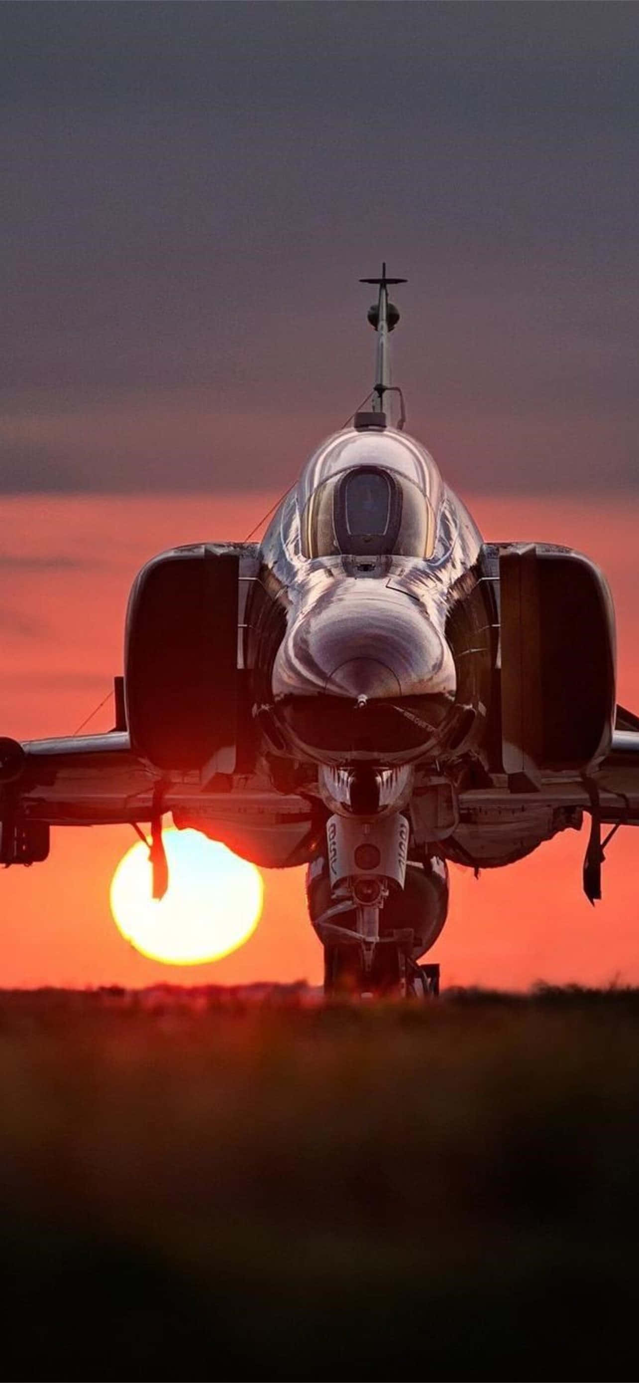 飛機前視圖特寫 Android 背景 壁紙 — 一架戰鬥機面向前方，夕陽在它身後落下，在天空中投射出火熱的橙色和紅色色調。
