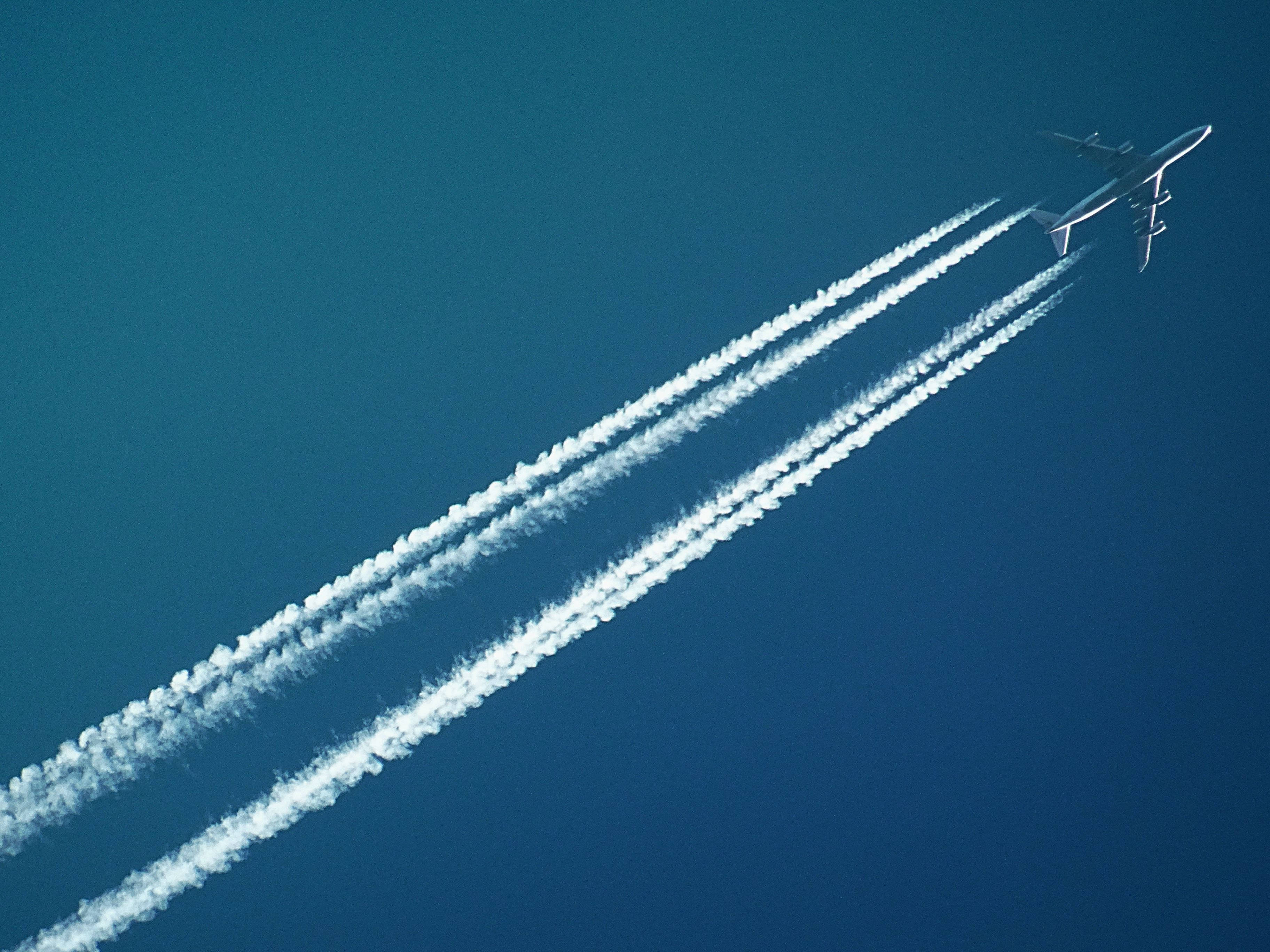 飛機劃出白煙線 壁紙 — 一架商用飛機在晴朗的藍天中翱翔，留下三條清晰的白色彩虹雲。