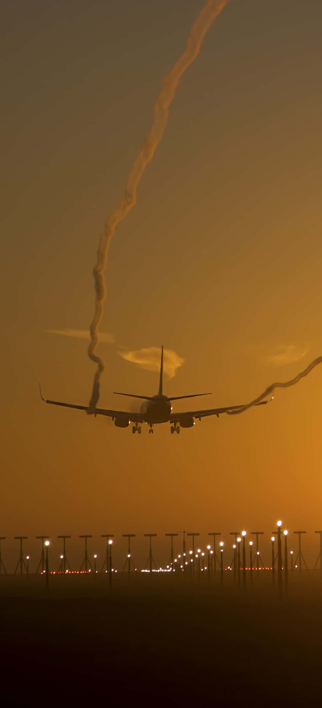 飛機即將降落安卓飛機壁紙 壁紙 — 一架商用飛機在火紅橙色日落映襯下，輪廓分明，正朝向燈光閃爍的跑道下降。
