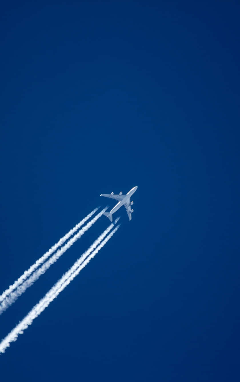 飛機在夕陽天空中迷人掠過 壁紙 — 一架白色客機在深藍色的天空中翱翔，身後留下三條清晰的白色凝結尾跡。
