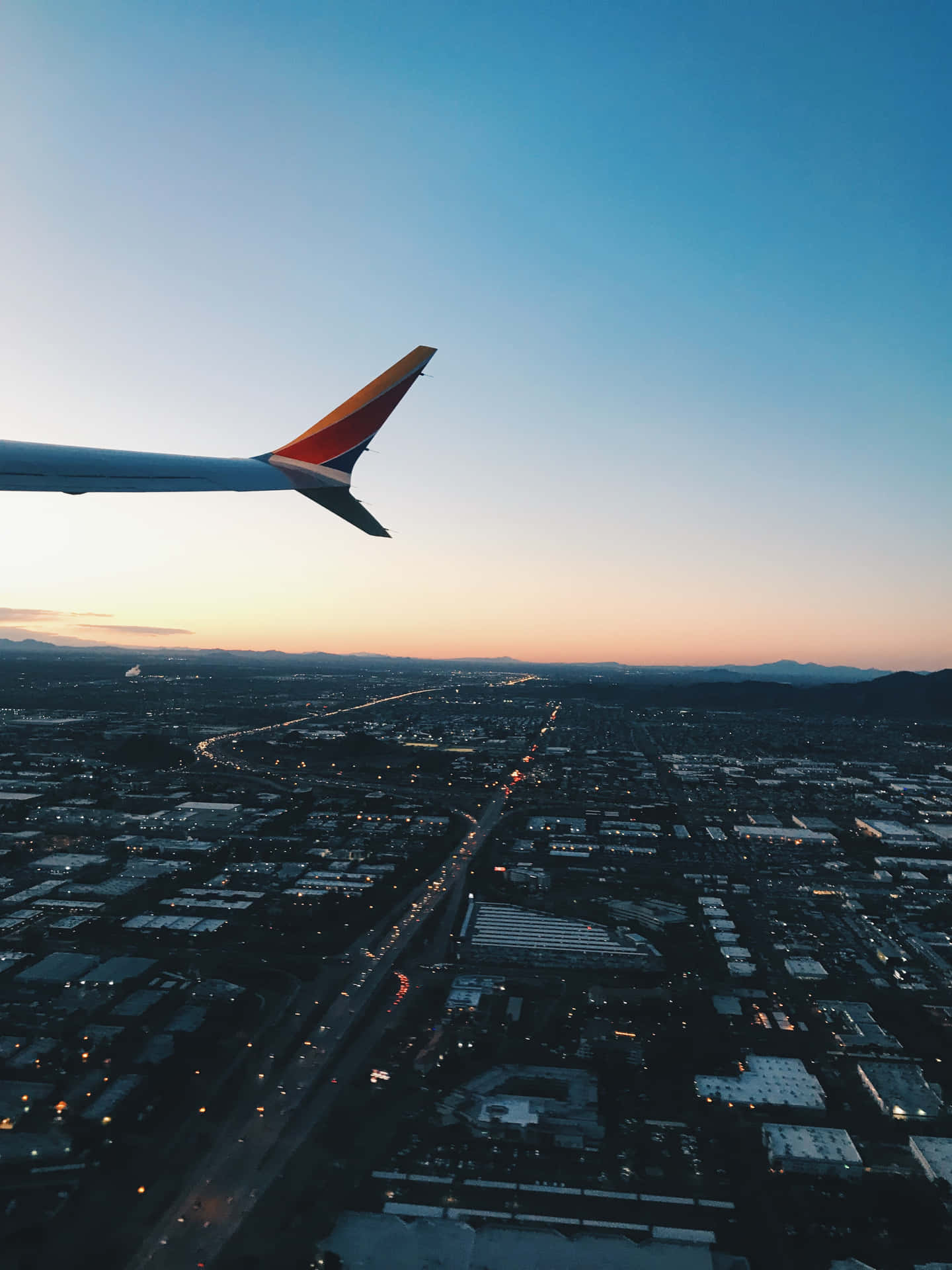 日落時分城市上空的飛機機翼，閃爍的街道和山脈