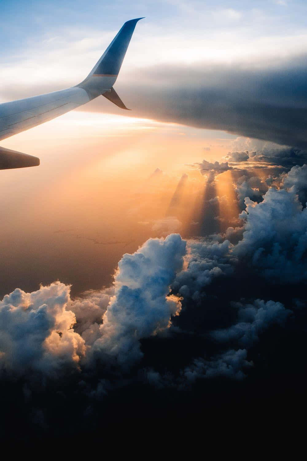 飛機尾翼與天空背景 壁紙 — 從飛機窗戶看到陽光穿過雲層，機翼在畫面中。
