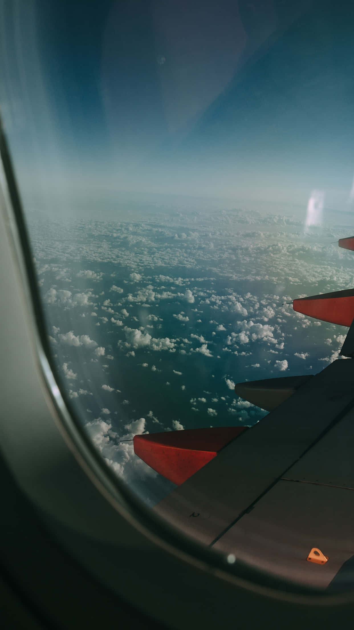飛機從iPhone飛向天空 壁紙 — 從飛機窗戶看到的紅色尖端飛機機翼，俯瞰下方無盡的白雲和藍天。