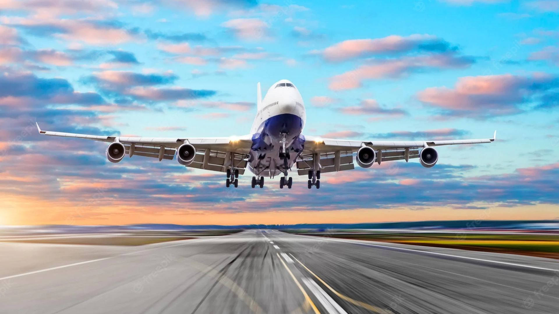 飛機從跑道起飛 壁紙 — 一架大型客機在充滿活力的日落天空（帶有粉紅色和藍色雲彩）背景下從跑道起飛。