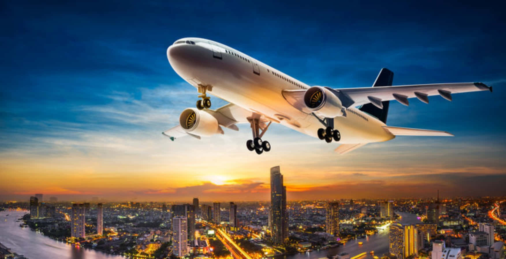 一架商用飛機在日落時低飛過城市，下方是燈火通明的建築物和河流。