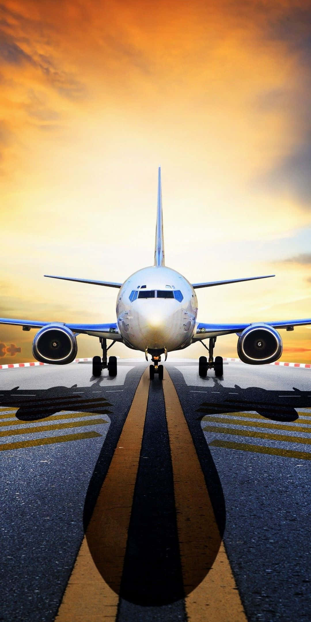 飛機掠過絢麗夕陽天空的空中視角 壁紙 — 一架商用飛機在火紅橙黃色的日落天空下，在跑道上向前。
